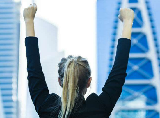 The back of a young woman wearing black professional clothes and raising her hands.