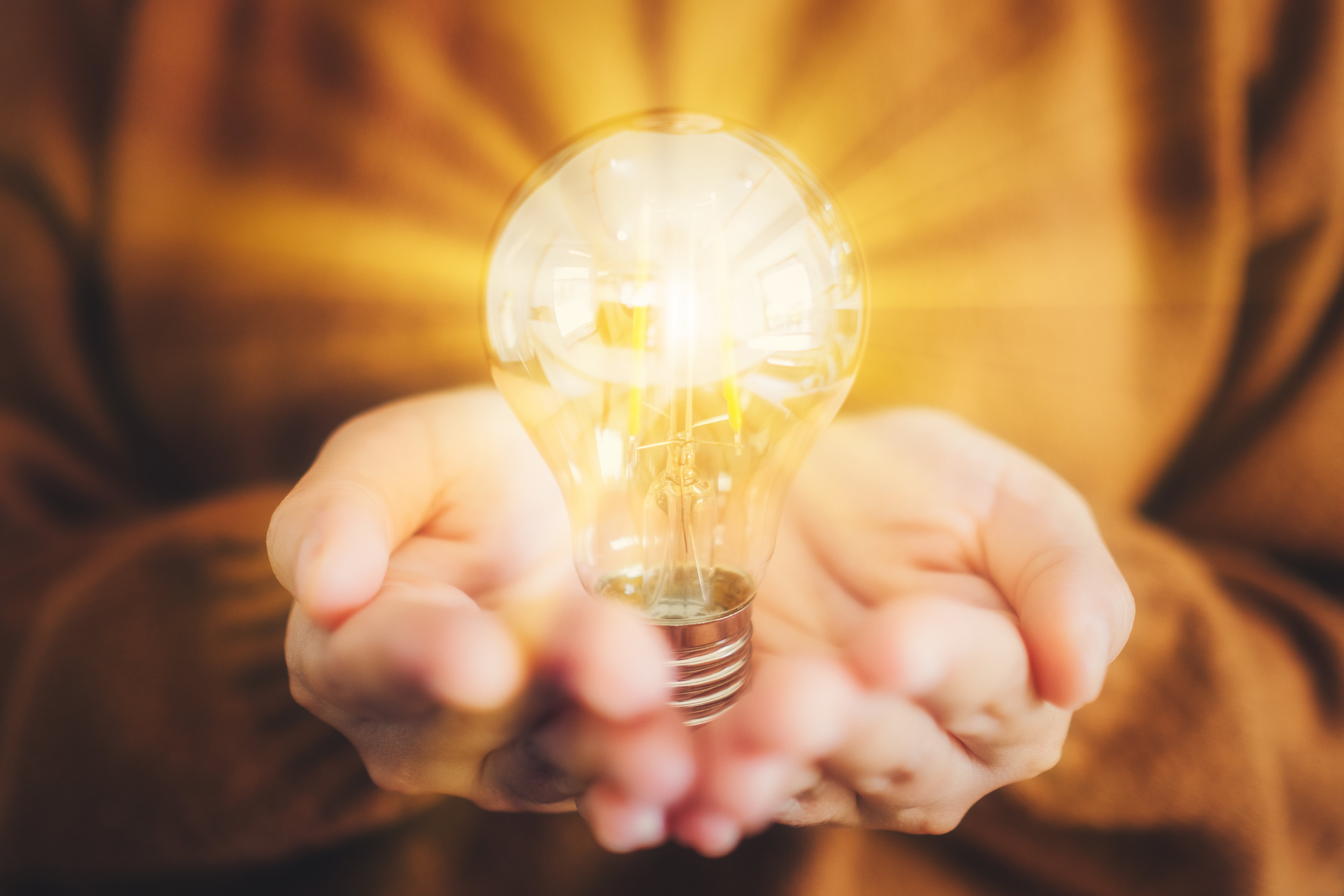 Closeup image of hands holding a glowing light bulb